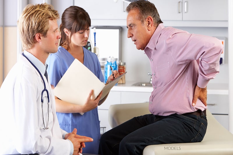 Middle-aged man talking to a doctor and nurse while holding his painful back